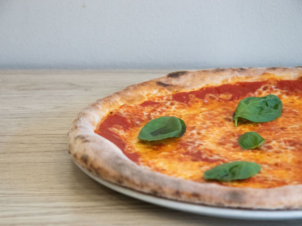 Margherita pizza s bosiljkom na tanjuru, na drvenom stolu.