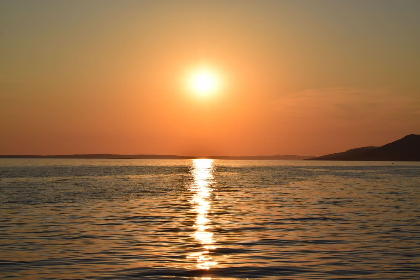 Zalazak sunca nad Jadranom u Starigradu, s niskim otočnim grebenom na obzoru.